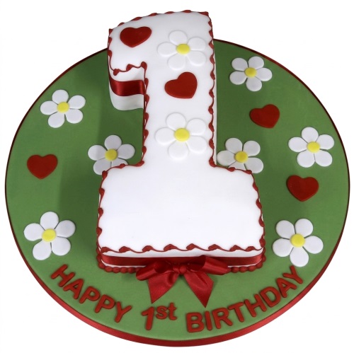 Number one shaped cake for a 1st birthday, decorated with white daisies, red hearts, and a red ribbon on a green cake board.