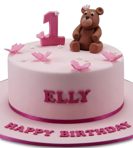 Pink birthday cake with a brown teddy bear, pink number one, and pink butterflies.