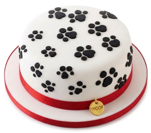 Round white cake with black paw prints, red ribbon, and a gold "WOOF" tag.