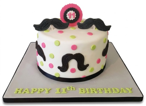 White round birthday cake with black mustaches, pink and green polka dots, and a custom age topper.