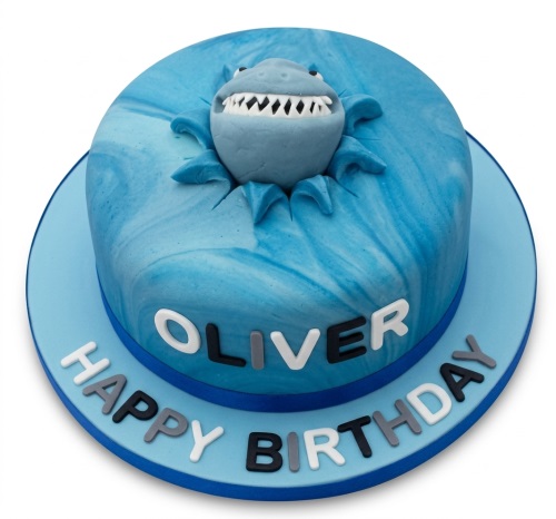 Round blue marbled cake with a 3D shark head emerging from the top, featuring a personalised name and 'Happy Birthday' message.