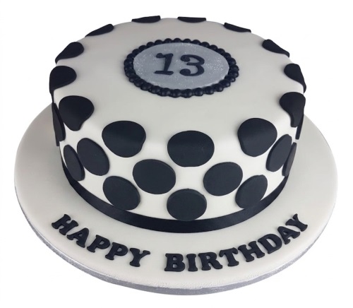 Round white cake with black polka dots, black ribbon, and a silver plaque with a custom age.