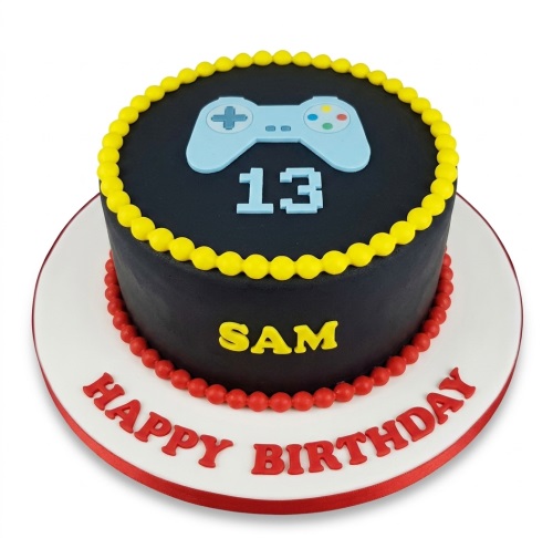 Round black cake with a light blue gaming controller on top, yellow and red beaded borders, and red 'Happy Birthday' message.