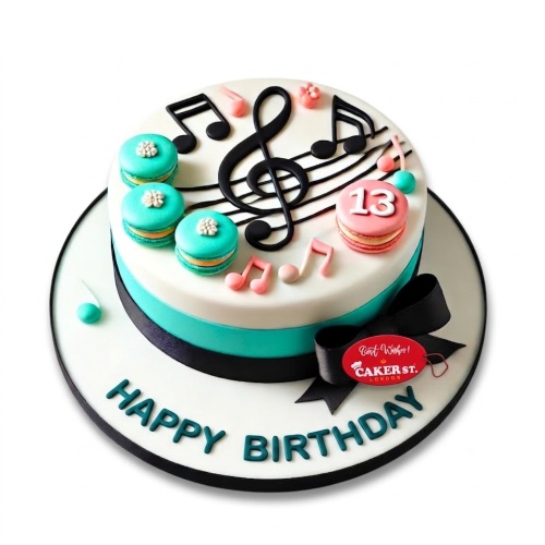 Round white and teal birthday cake with black musical notes, treble clef, and colourful macarons.