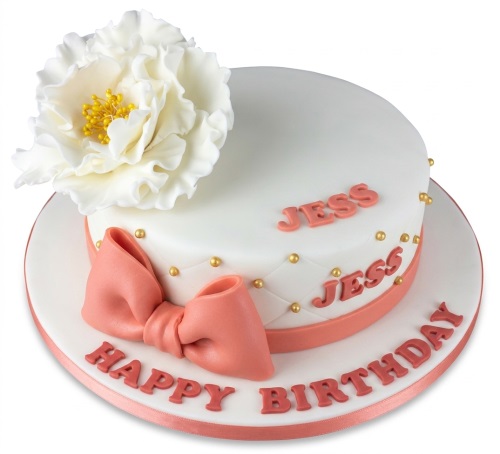White round birthday cake with a large white sugar flower, peach bow, gold edible pearls, and 'Happy Birthday' message.
