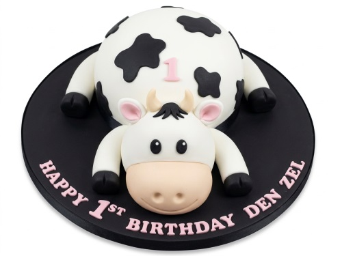 White and black 3D cow cake with a pink number one on its back, on a black cake board.