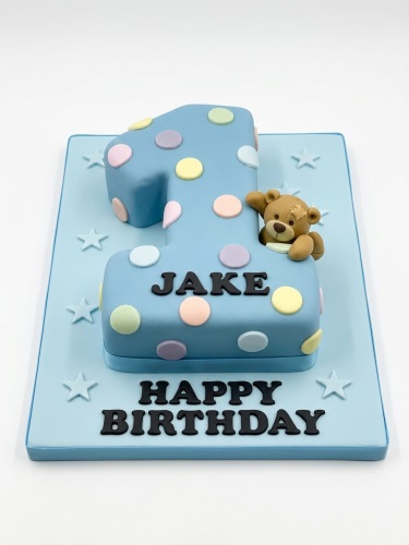 Blue number one cake with pastel polka dots and a brown teddy bear, for a first birthday.