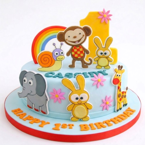 Light blue 1st birthday cake decorated with a yellow number one, rainbow, elephant, monkey, snail, rabbits, and giraffe.