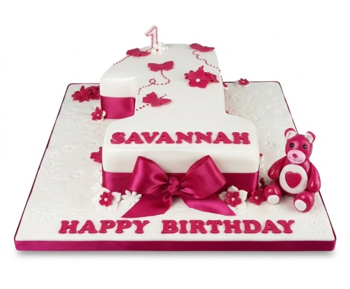 White number one shaped cake with pink teddy bear, butterflies, flowers, and ribbon for a 1st birthday.