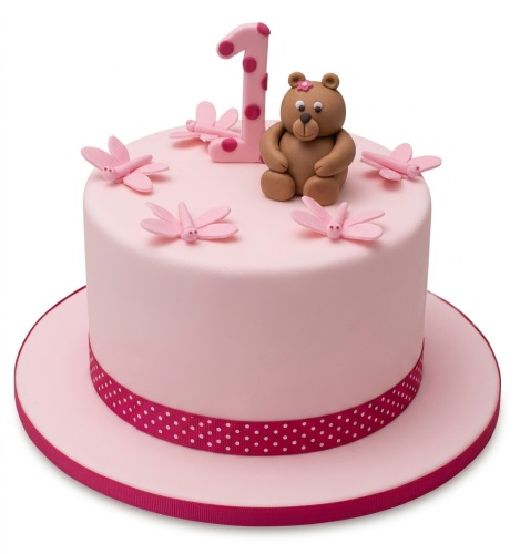 Pink round cake with a brown teddy bear, pink number one topper, and pink dragonfly decorations.