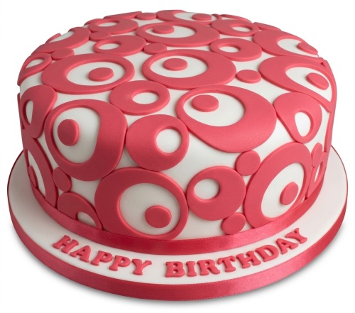 Round white fondant cake decorated with coral pink circles and a 'Happy Birthday' message.