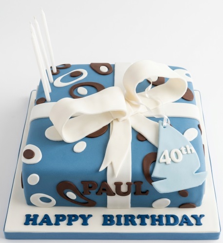 Square blue gift box birthday cake with white ribbon, bow, brown and white patterns, and a light blue custom age tag.