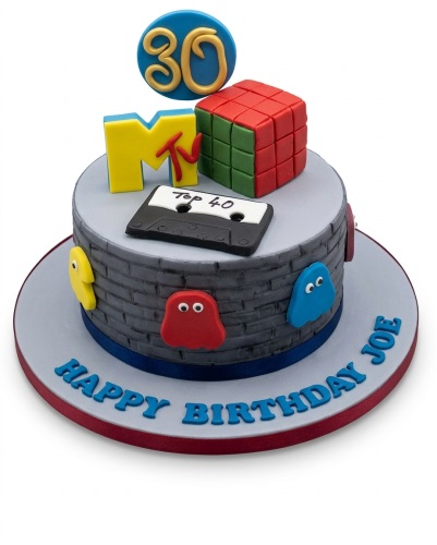 Two-tier retro themed birthday cake with a custom age topper, MTV logo, Rubik's Cube, cassette tape, and ghost characters.