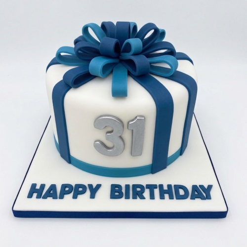 White round birthday cake decorated like a gift box with blue ribbons and a silver custom age '31' topper.