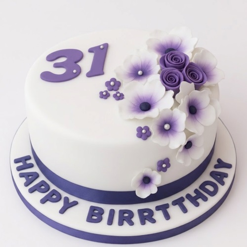 White round birthday cake with purple and white sugar flowers, custom age topper, and "Happy Birthday" message.
