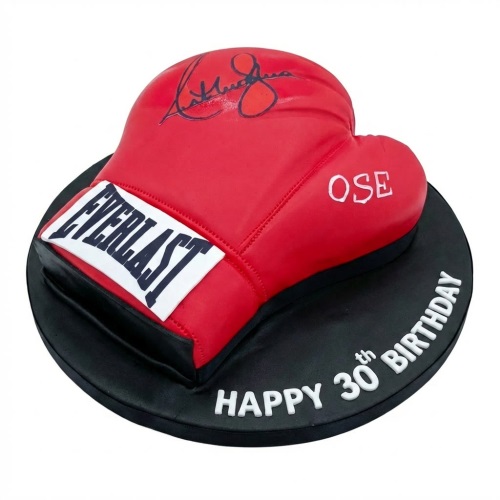 Red boxing glove shaped birthday cake with black base and white lettering.
