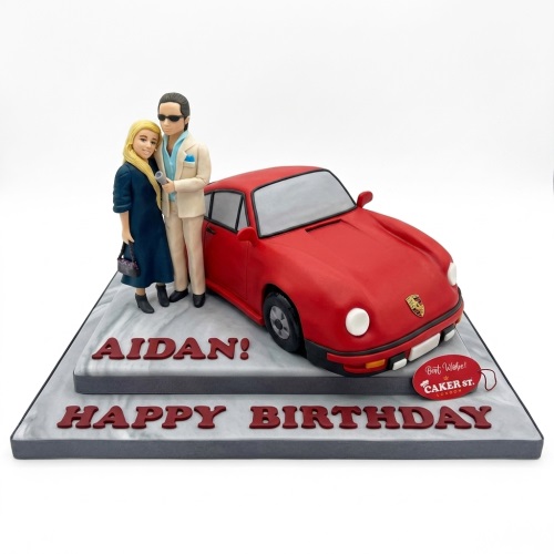 Red sports car cake with male and female figures and 'Happy Birthday' message.