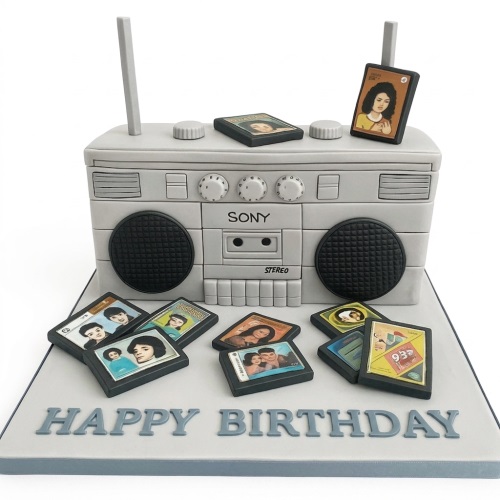 Grey boombox birthday cake with black speakers and personalised photo cassette tapes, 'Happy Birthday' message on board.