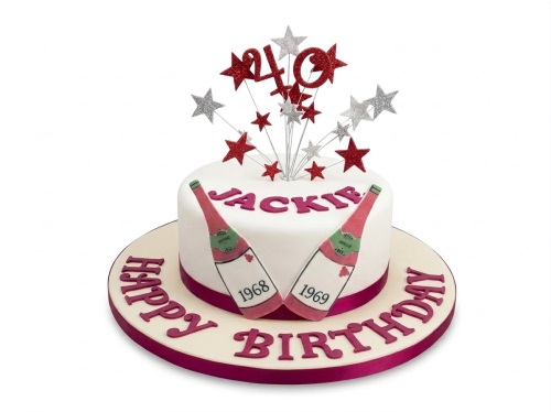 White round birthday cake with red and silver star toppers, champagne bottles, and custom message.