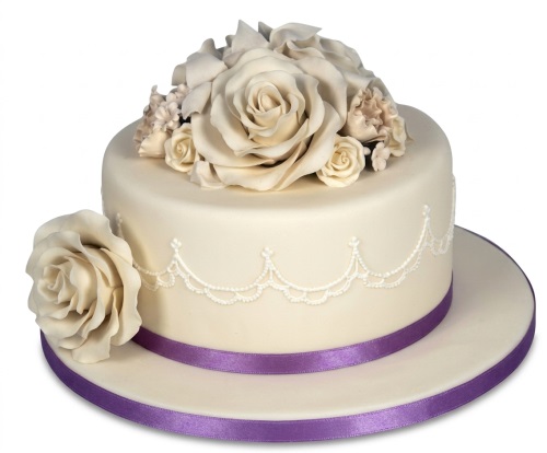 Elegant cream floral birthday cake with sugar roses, white piping, and a purple ribbon.