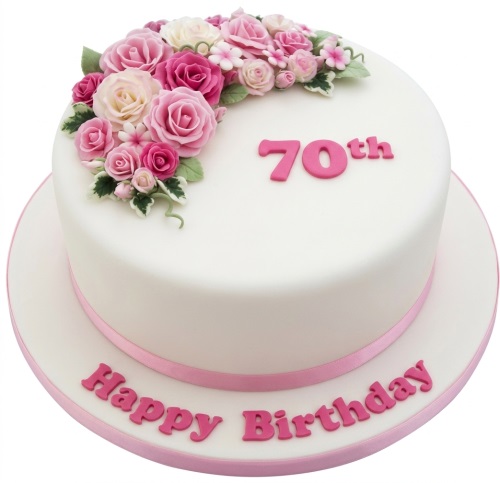 Round white birthday cake with pink sugar roses, green leaves, and a pink ribbon.
