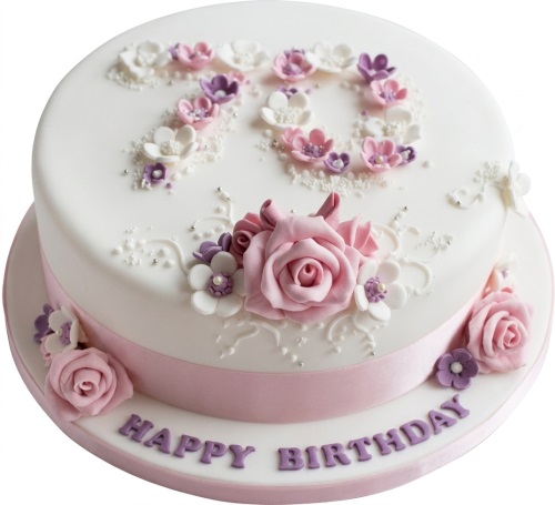 White round 70th birthday cake with pink and purple sugar flowers, silver beads, and "Happy Birthday" message.