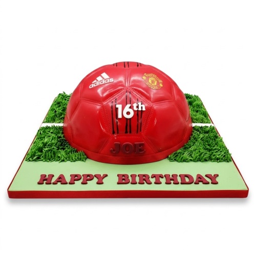 Red football shaped cake with Manchester United logo, Adidas logo, green grass, and custom age and name area.