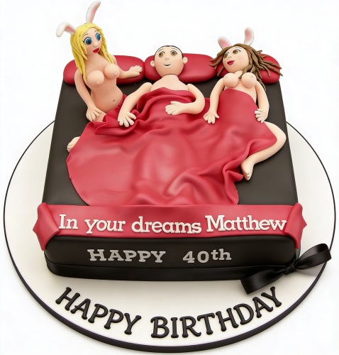Novelty birthday cake with a man in bed with two women wearing bunny ears, featuring a custom message ribbon.