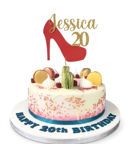 Round white and pink drip cake with macarons, raspberries, and a red high heel topper.
