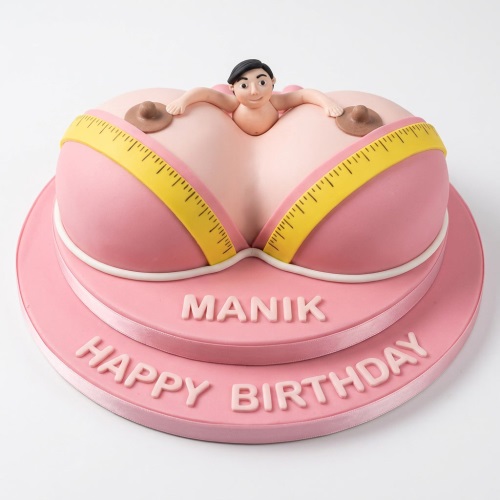 Pink novelty birthday cake shaped like a bra with a small man figure emerging, and a measuring tape design.