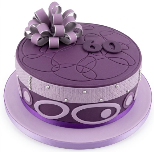 Round purple fondant birthday cake with a large bow, silver pearls, and custom age topper.