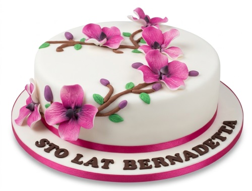 Round white birthday cake with pink magnolia flowers, green leaves, and a pink ribbon.