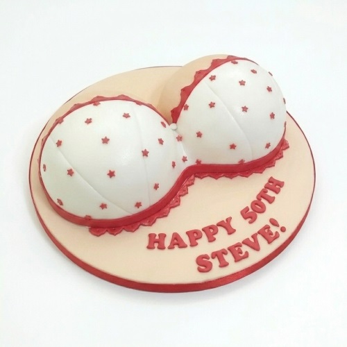 White bra shaped cake with red stars and lace trim on a peach cake board.