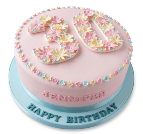 Pink birthday cake with pastel sugar flowers, custom age topper, and a blue ribbon.