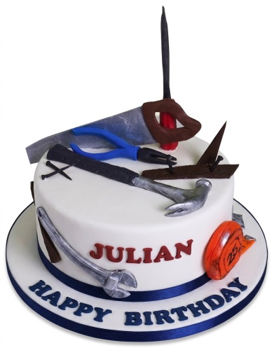 White round birthday cake decorated with edible construction and DIY tools, blue ribbon, and a custom name.