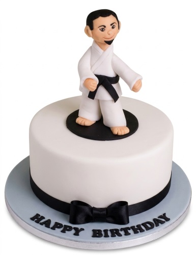 Round white birthday cake with a black belt martial artist figure and a black ribbon bow.