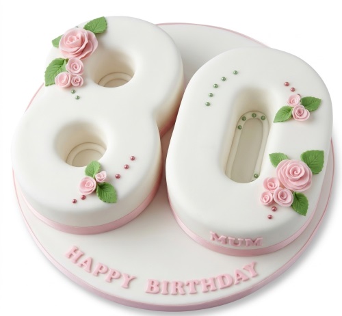 White number cake with pink sugar roses, green leaves, and pink edible pearls.