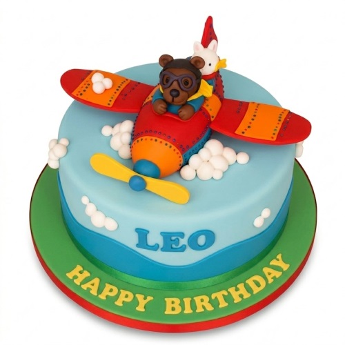 Round blue birthday cake with red airplane, bear pilot, rabbit, and white clouds, personalised name and 'Happy Birthday' message.