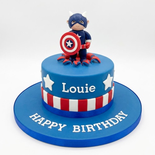 Blue Captain America style birthday cake with figurine topper, white stars, and red and white stripes.
