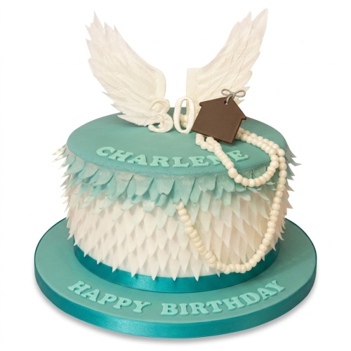 Round teal and white birthday cake with angel wings, feather texture, and edible pearls.