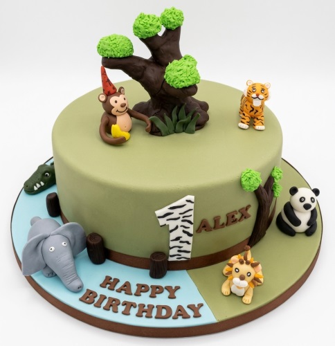Round green fondant cake with a tree, monkey, tiger, crocodile, elephant, panda, and lion figurines, with a zebra print number one topper and 'Happy Birthday' message.