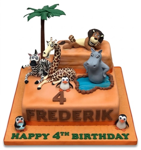 Two-tier Madagascar theme birthday cake with edible lion, zebra, giraffe, hippo, and penguins, a palm tree, and custom age topper.