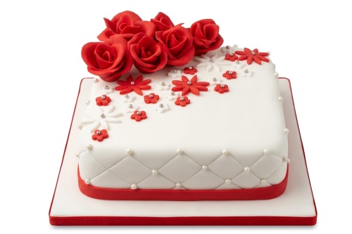 White square cake with red sugar roses, red and white flowers, and edible pearls.