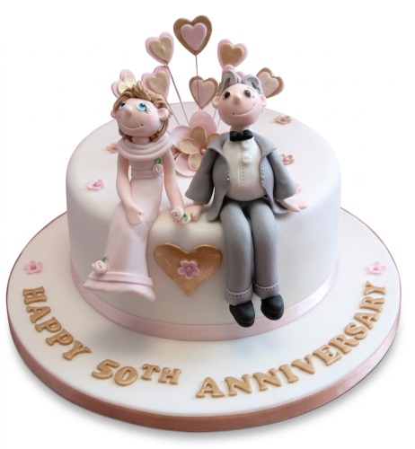 White round cake with fondant couple figures, pink and gold hearts, and 'Happy 60th Anniversary' text on the board.