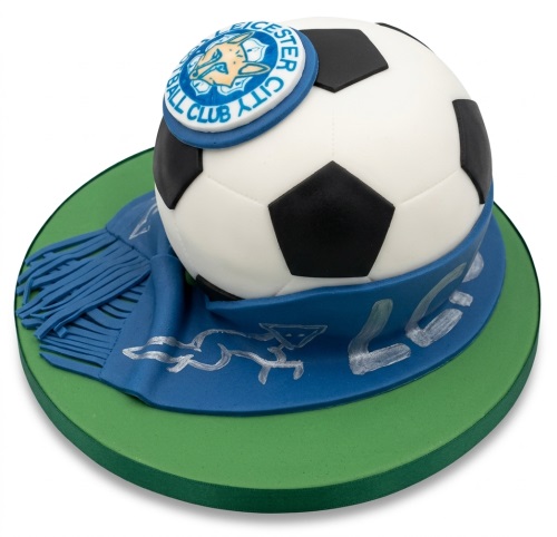 3D football cake with a Leicester City Football Club badge and a blue scarf on a green cake board.