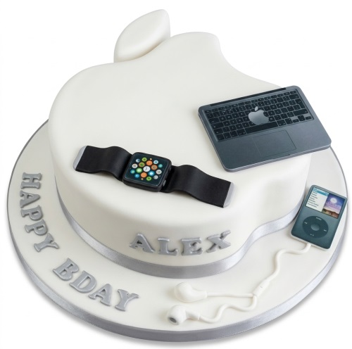 White two-tier cake shaped like an Apple logo, decorated with edible laptop, smartwatch, and music player, with a custom message on the board.