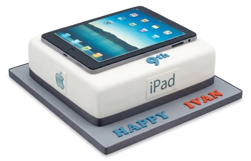 White square birthday cake with an edible iPad image on top, an Apple logo, 'iPad' text, and custom age '9th' and 'Happy Ivan' text on the board.