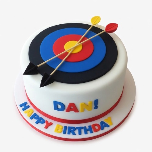 Round white birthday cake with an edible archery target and two crossed arrows on top. Custom message 'Happy Birthday' on the side.