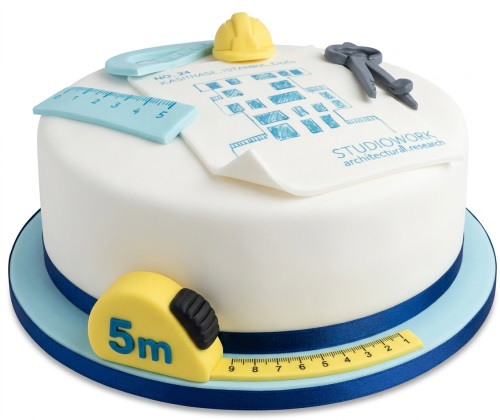 Round white cake with edible architect tools, blueprint, hard hat, ruler, compass, and tape measure.