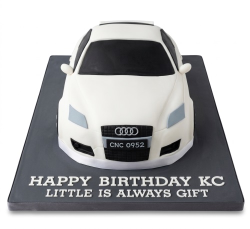 3D white Audi car shaped birthday cake on a grey board with custom message.